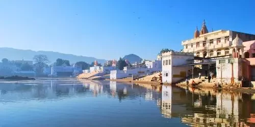 Pilgrims and travelers gathering at the sacred steps of the ghats surrounding the holy waters of Pushkar Lake during a peaceful sunset in Rajasthan.